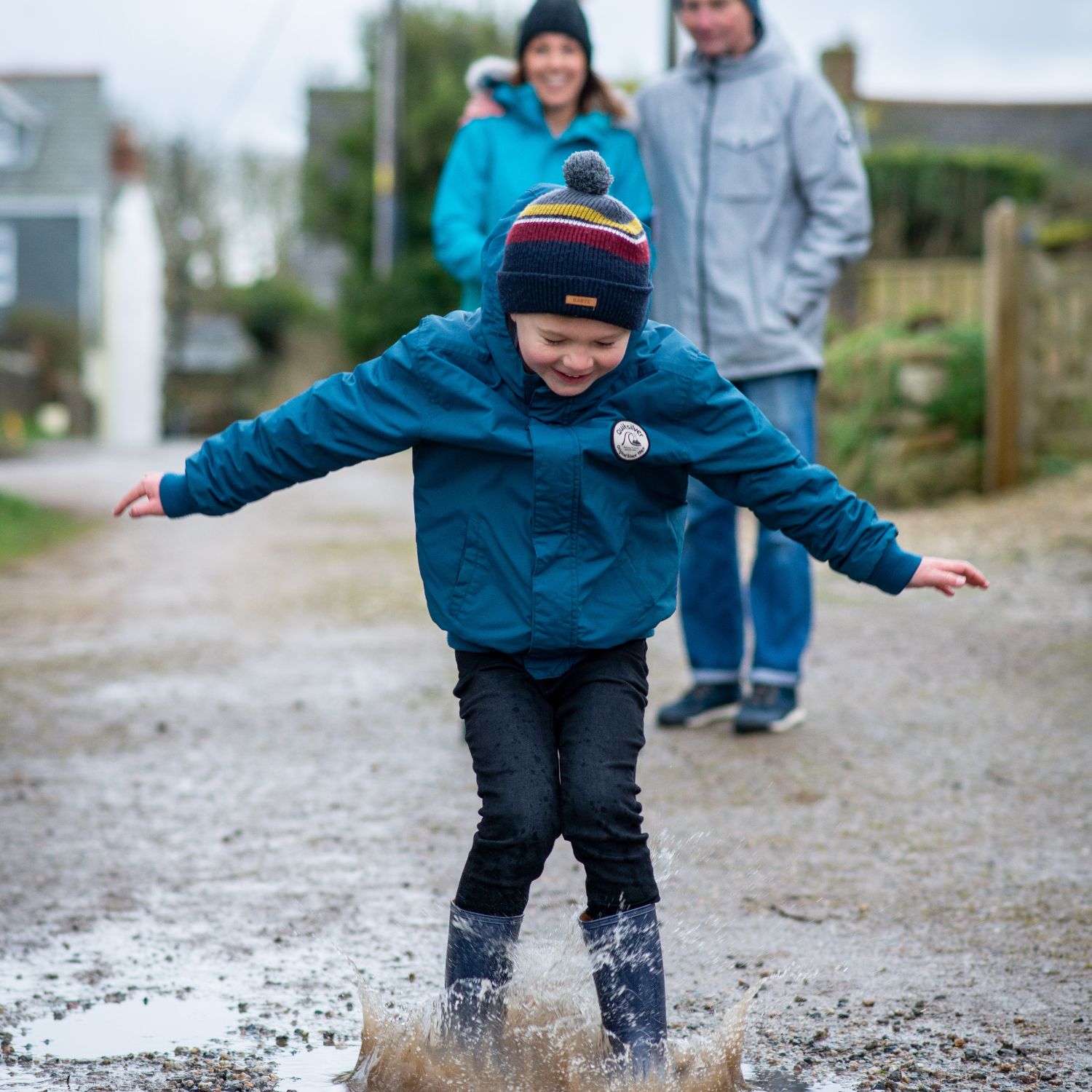 A young boy jumping in a puddle in front of his parents