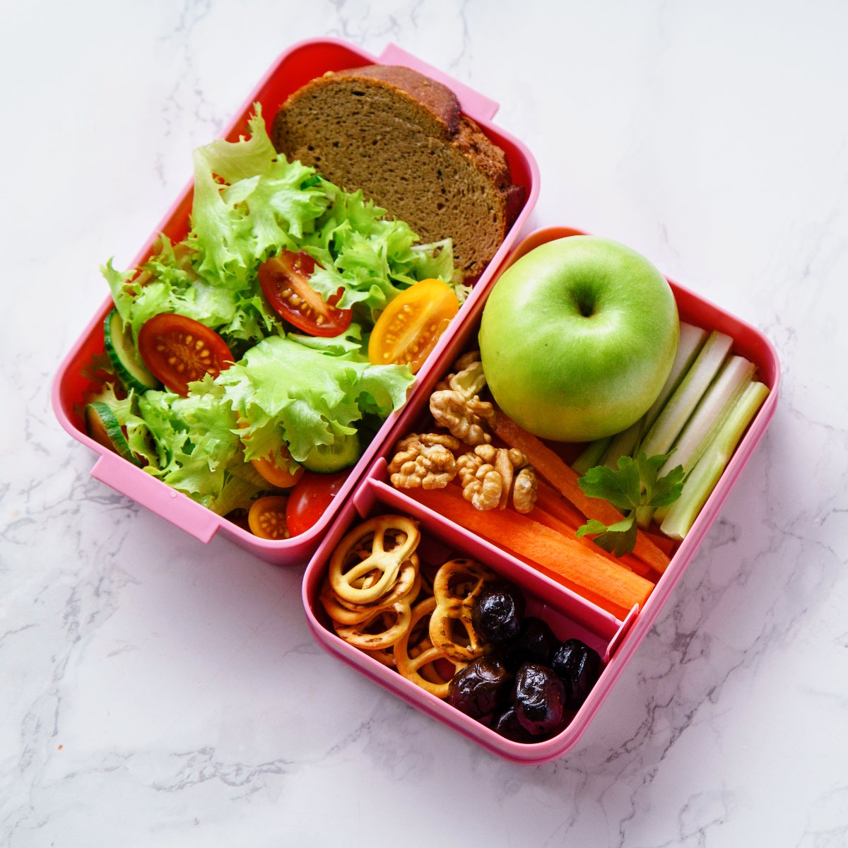 A lunch box full of snacks, including salad, pretzels, nuts and an apple